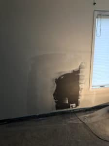Drywall with a light shining on it with plastic over carpet